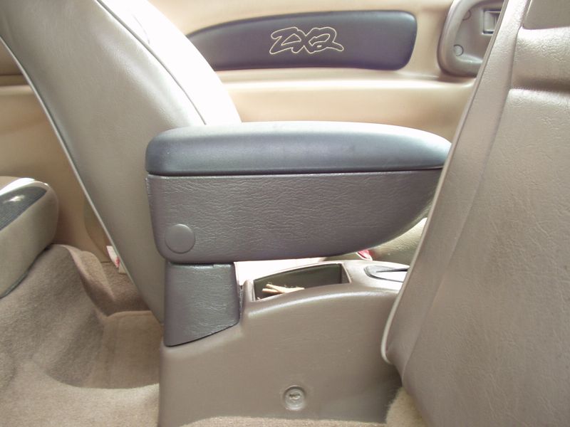 Black center armrest mounted between the front seats of a ZX2 with tan leather, a ZX2 logo on the door panel behind